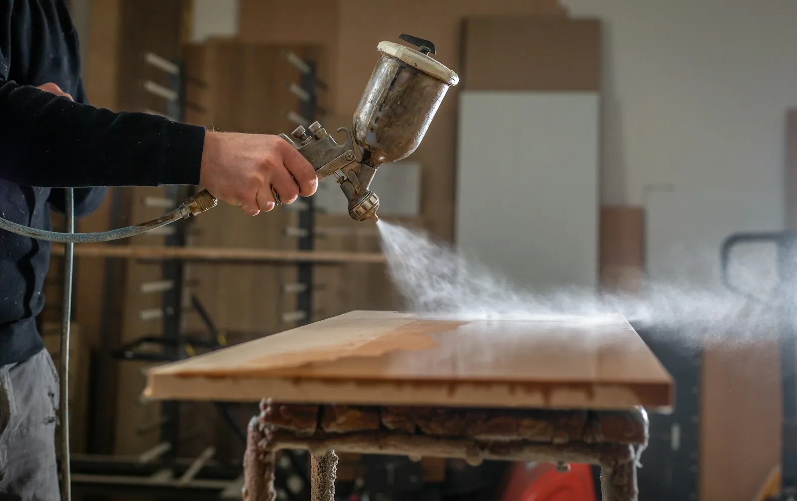 Aplicación de acabado con pistola sobre un tablero de madera.