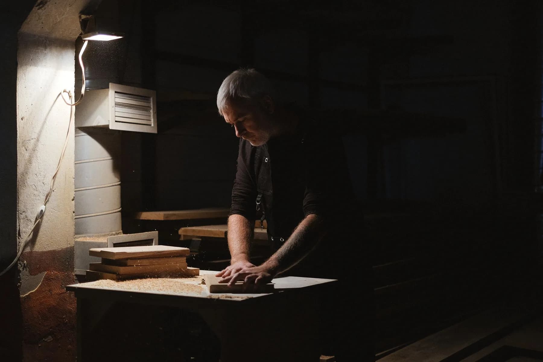 Artesano trabajando una pieza de madera en un banco iluminado en un taller oscuro.